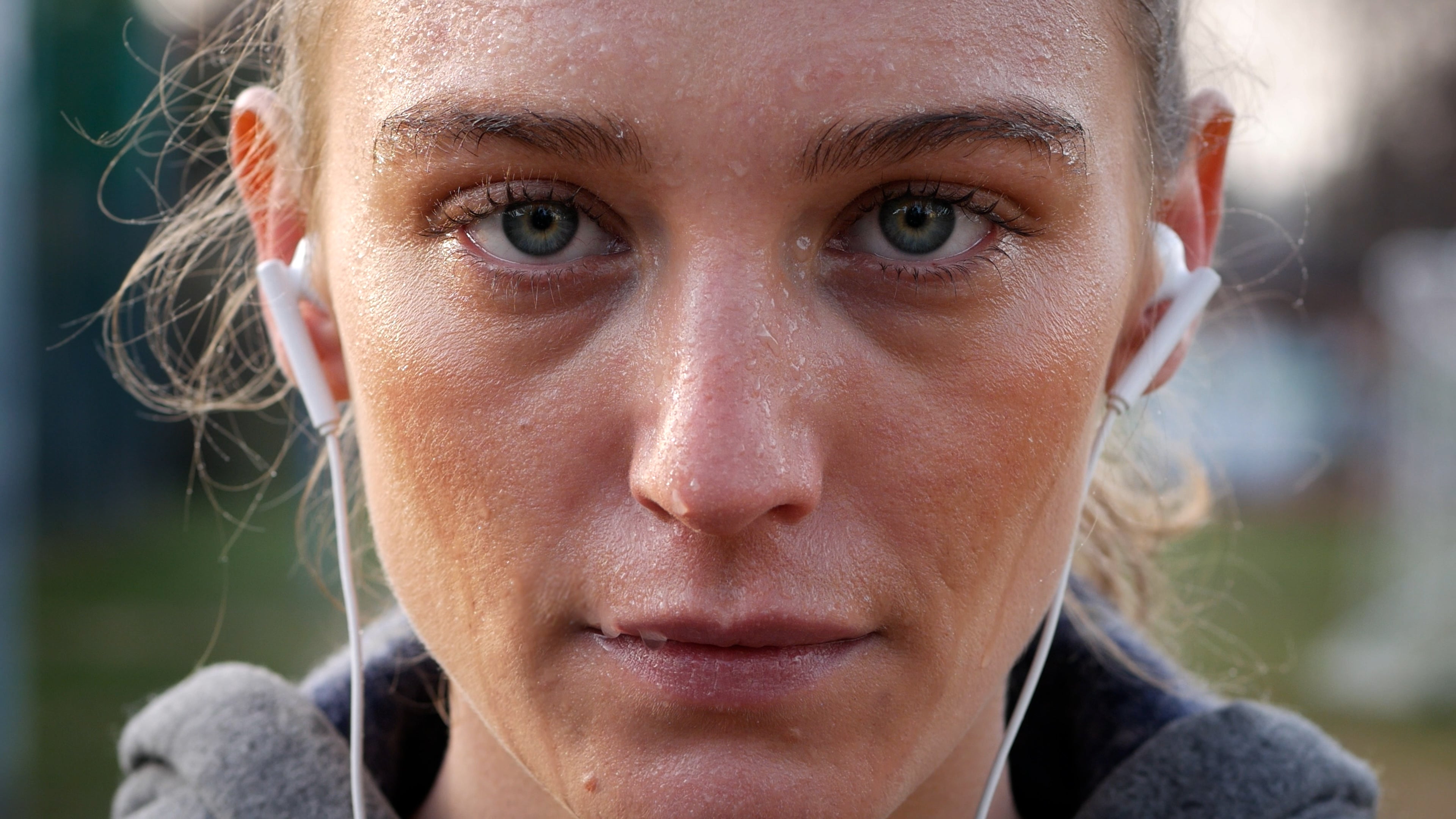 A close-up portrait of a woman with wet, sweaty skin and earphones in her ears after a workout.