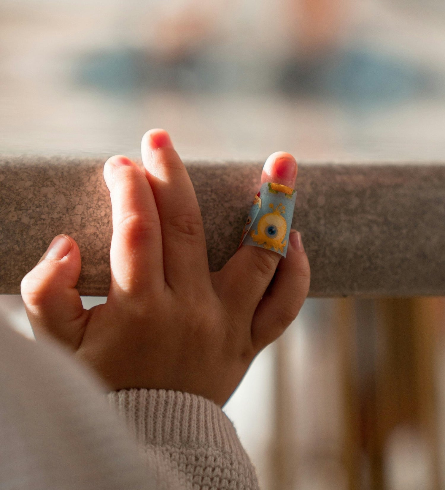 A close-up of a child's hand holding a railing, with a colorful adhesive bandage on one of their fingers.