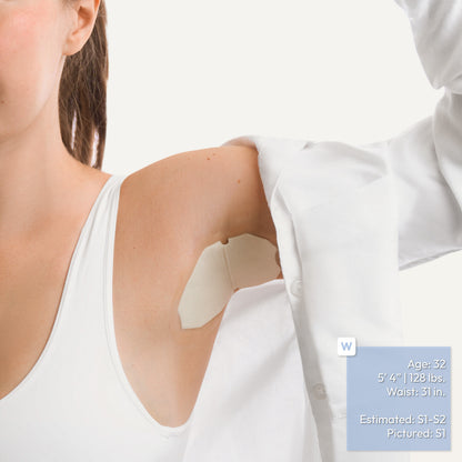 A close-up of a woman's upper arm and shoulder showing an underarm adhesive patch applied to the skin, with a white sleeve being lifted to reveal the patch. A small blue text box with body measurements appears in the lower right corner.