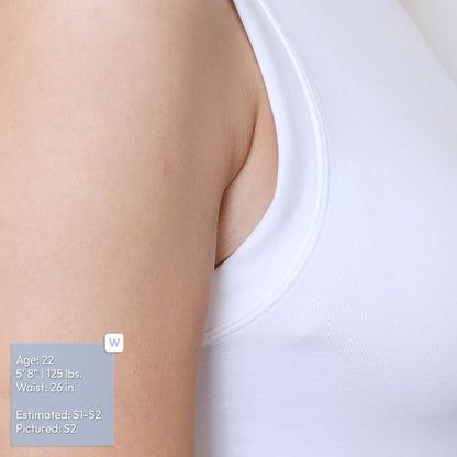 Close-up of a person's upper torso wearing a white ribbed tank top, with an underarm adhesive patch nestled in between her lowered arm and torso. A size/fit label overlay in the lower left corner.